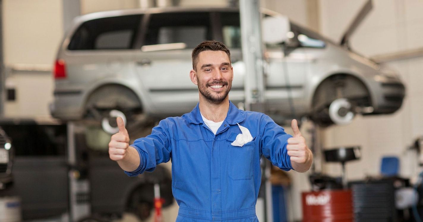 Smiling mechanic giving thumbs up in front of an SUV on the lift