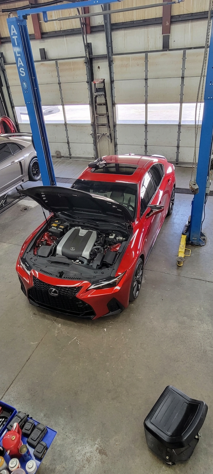 Red Lexus sport sedan with hood open being serviced on a lift